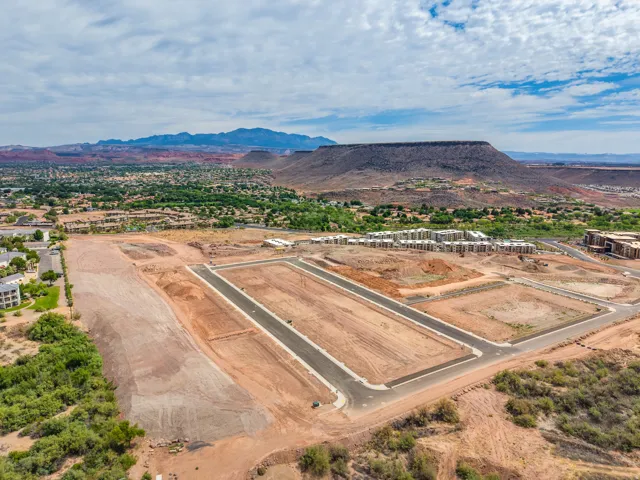 Developing residential plots with paved road infrastructure, surrounded by a verdant landscape and distant mountainous terrain