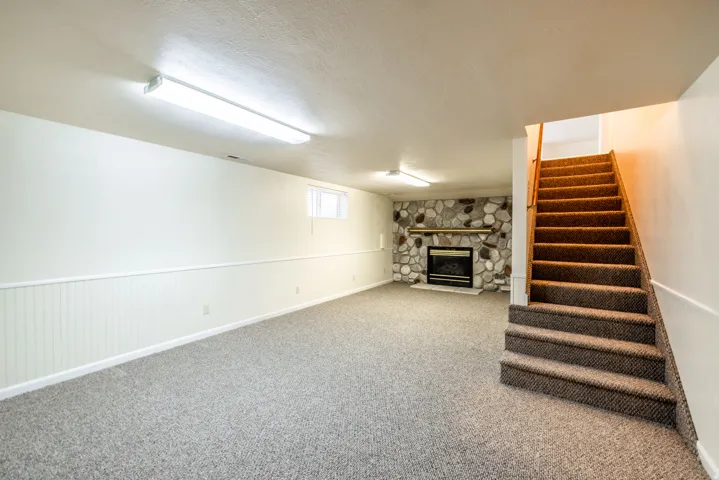 Spacious room featuring carpeting, wainscoting, and a stone-clad fireplace with a black insert