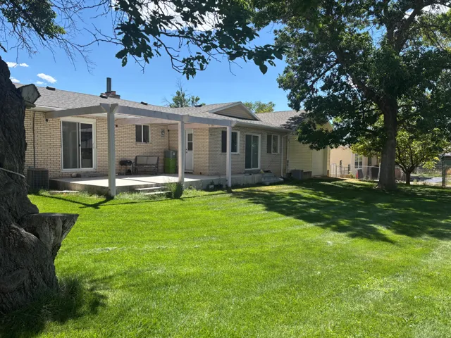 Expansive green lawn, brick exterior, concrete patio with pergola, mature trees, and sliding glass doors