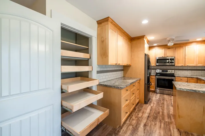 Chef's kitchen showcasing warm wood cabinetry with pull-out drawers, granite countertops, stainless steel appliances, subway tile backsplash, and wood-finish flooring throughout