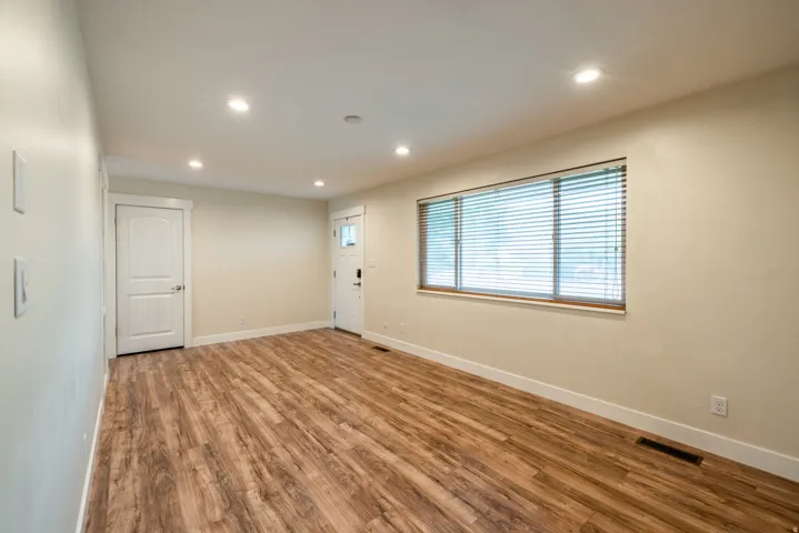 Bright, light-filled room showcasing rich wood-finish flooring, recessed ceiling lighting, and large windows with horizontal blinds