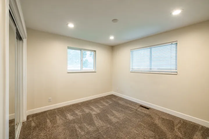 Recessed lighting, two windows with blinds, mirrored closet doors, and neutral carpeting