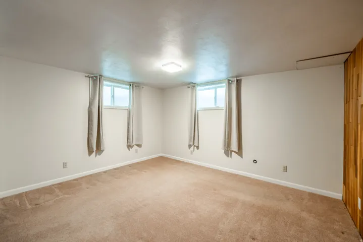 Spacious corner room flooded with natural light from multiple windows featuring neutral walls, neutral carpet flooring, and ceiling-mounted lighting fixture