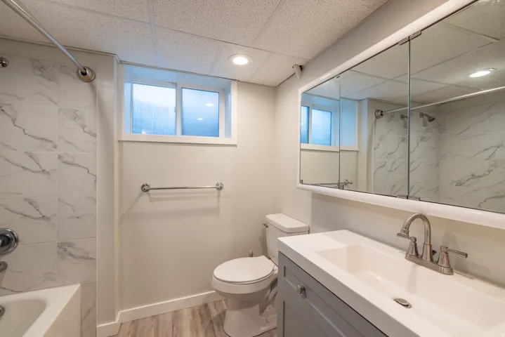 Full bathroom featuring a single vanity with storage, mirrored medicine cabinet, a toilet, a tub with a shower, and wood-finish flooring