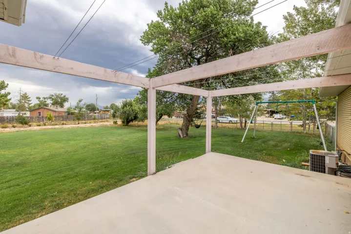 Concrete patio with an open pergola structure, expansive green lawn, and mature trees