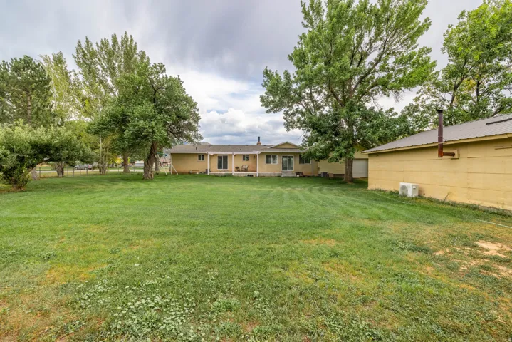 Expansive grounds featuring a mature tree-lined landscape and open lawn, with a single-story brick residence and detached garage situated on the property