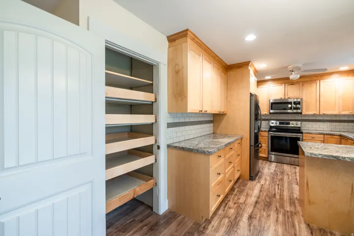 Kitchen featuring wood-finish flooring, light wood cabinetry, stainless steel appliances, and solid surface countertops