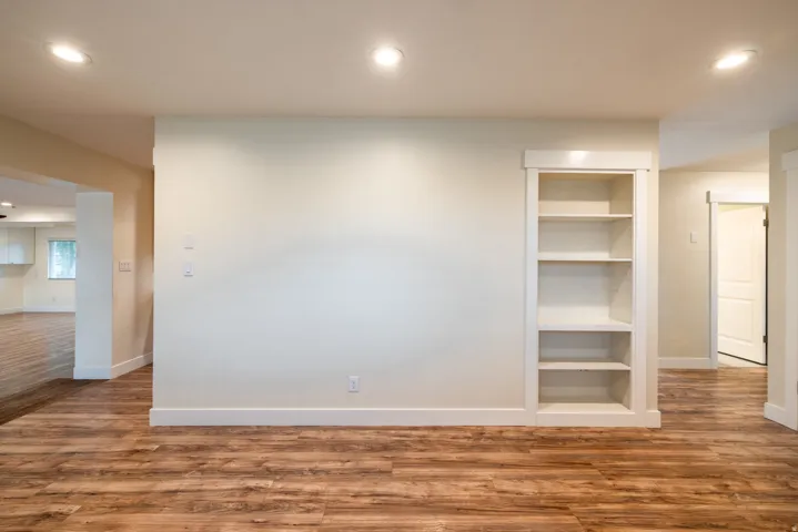 Wood-finish flooring, recessed ceiling lighting, built-in shelving, white trim, and a white interior door