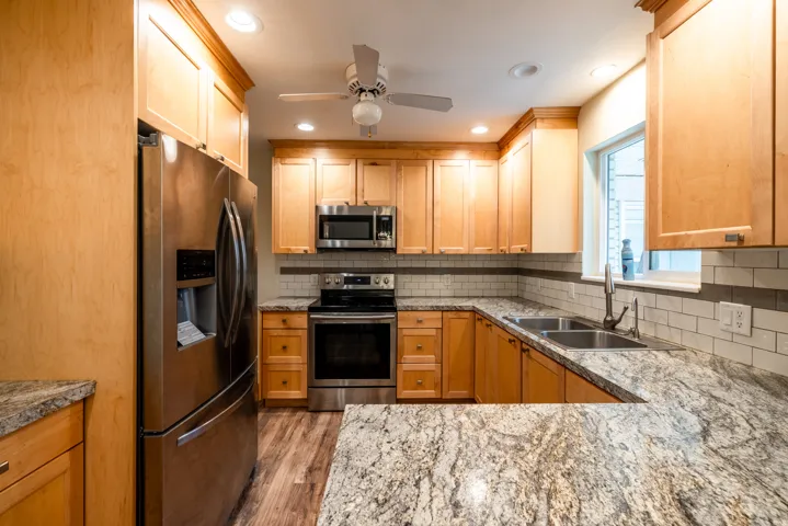 Light wood cabinetry, stainless steel appliances, dual basin sink, white subway tile backsplash, and stone-finish countertops