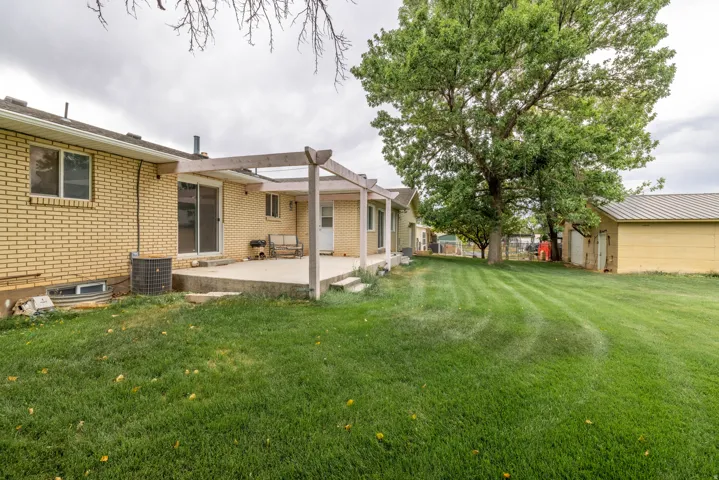 Expansive green lawn with mature trees, a concrete patio, a pergola structure, and a detached shop.