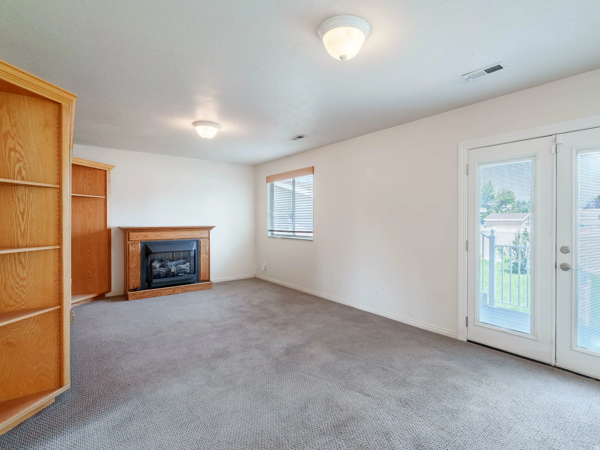 Spacious recreation room featuring neutral carpeting, wood-finish cabinetry, a built-in fireplace with wood surround, recessed ceiling lighting, and glass sliding doors providing natural light and access to outdoor space