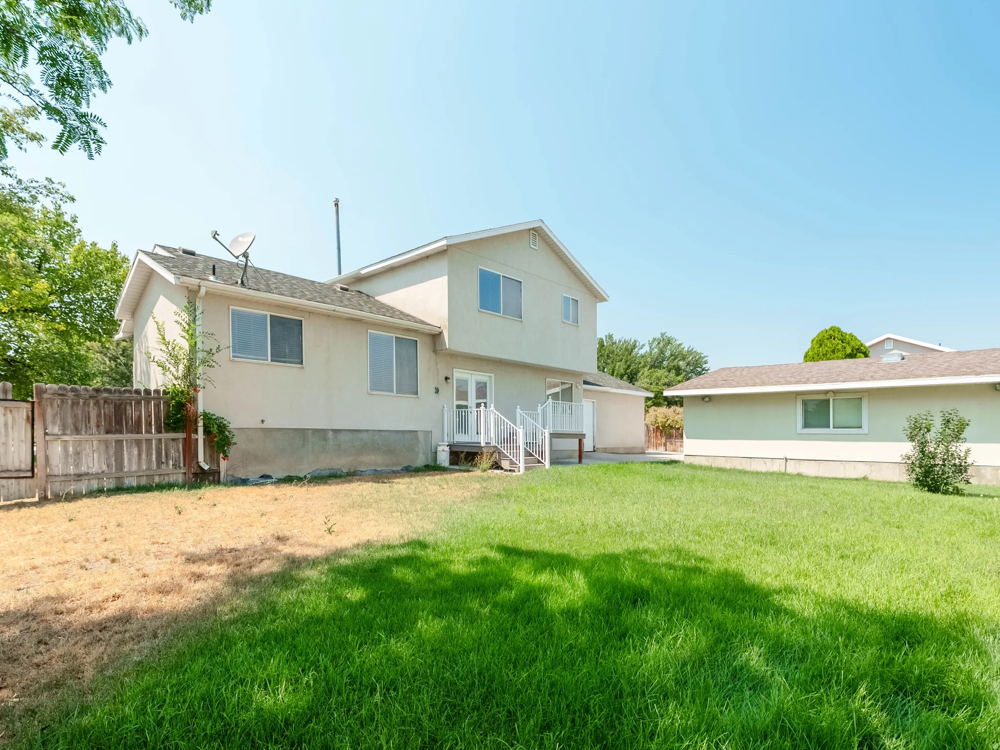 Spacious backyard featuring a manicured lawn with mature landscaping, wooden perimeter fencing, and a two-story residence with multiple windows and a rear deck entry