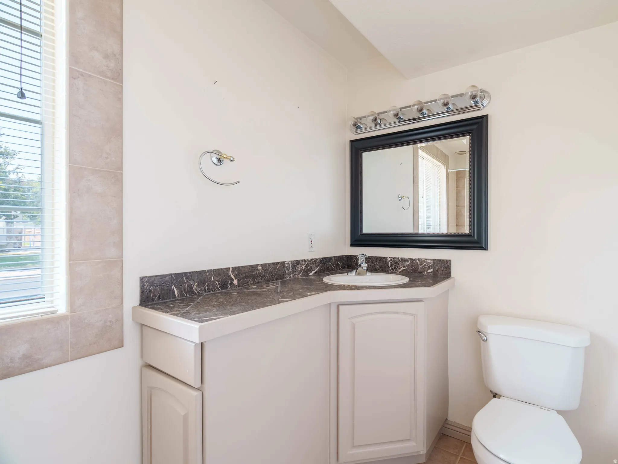 Vanity with a single basin sink, dark stone-look countertop, and white cabinetry