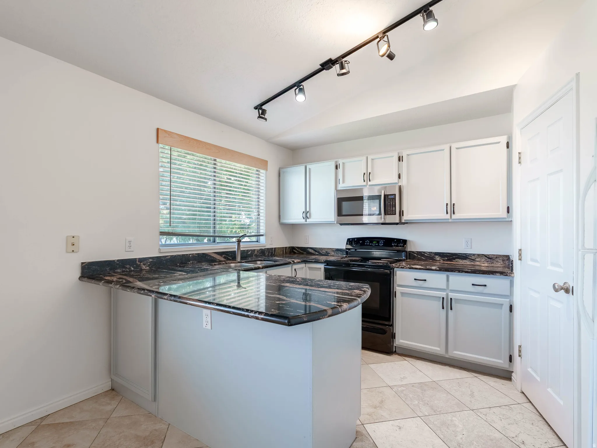 Kitchen featuring white cabinetry, black stone countertops, stainless steel microwave, black electric range, and track lighting