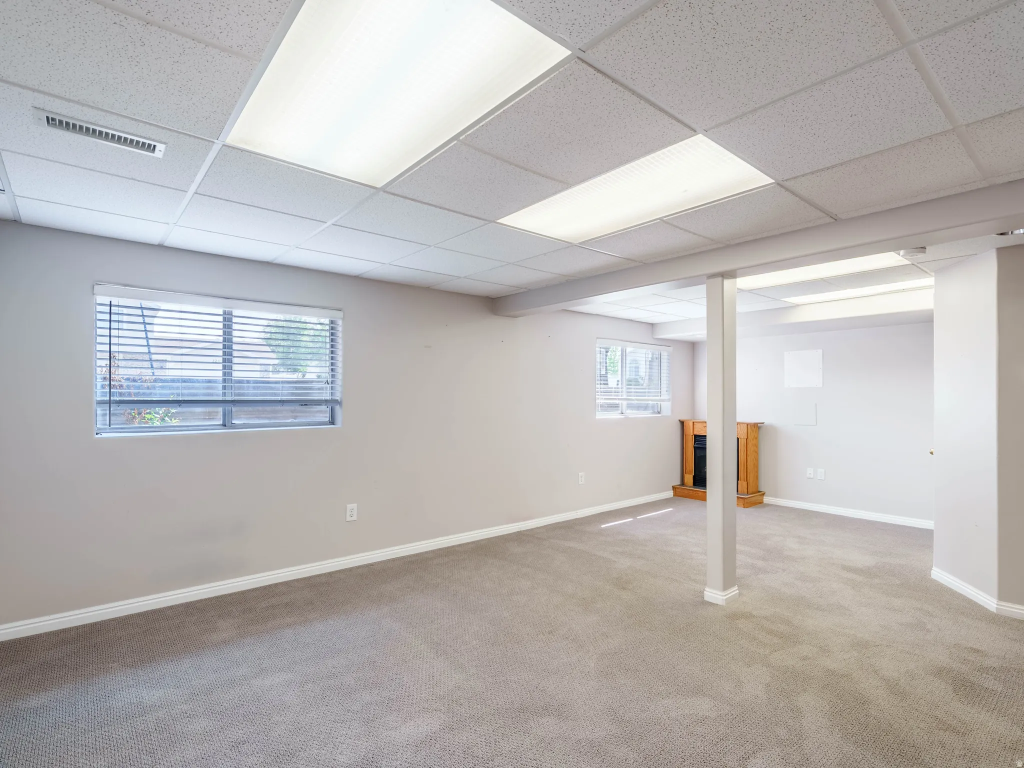 Bright, open office or studio space featuring recessed and linear ceiling panels, neutral wall finishes, carpeted flooring, and a support column