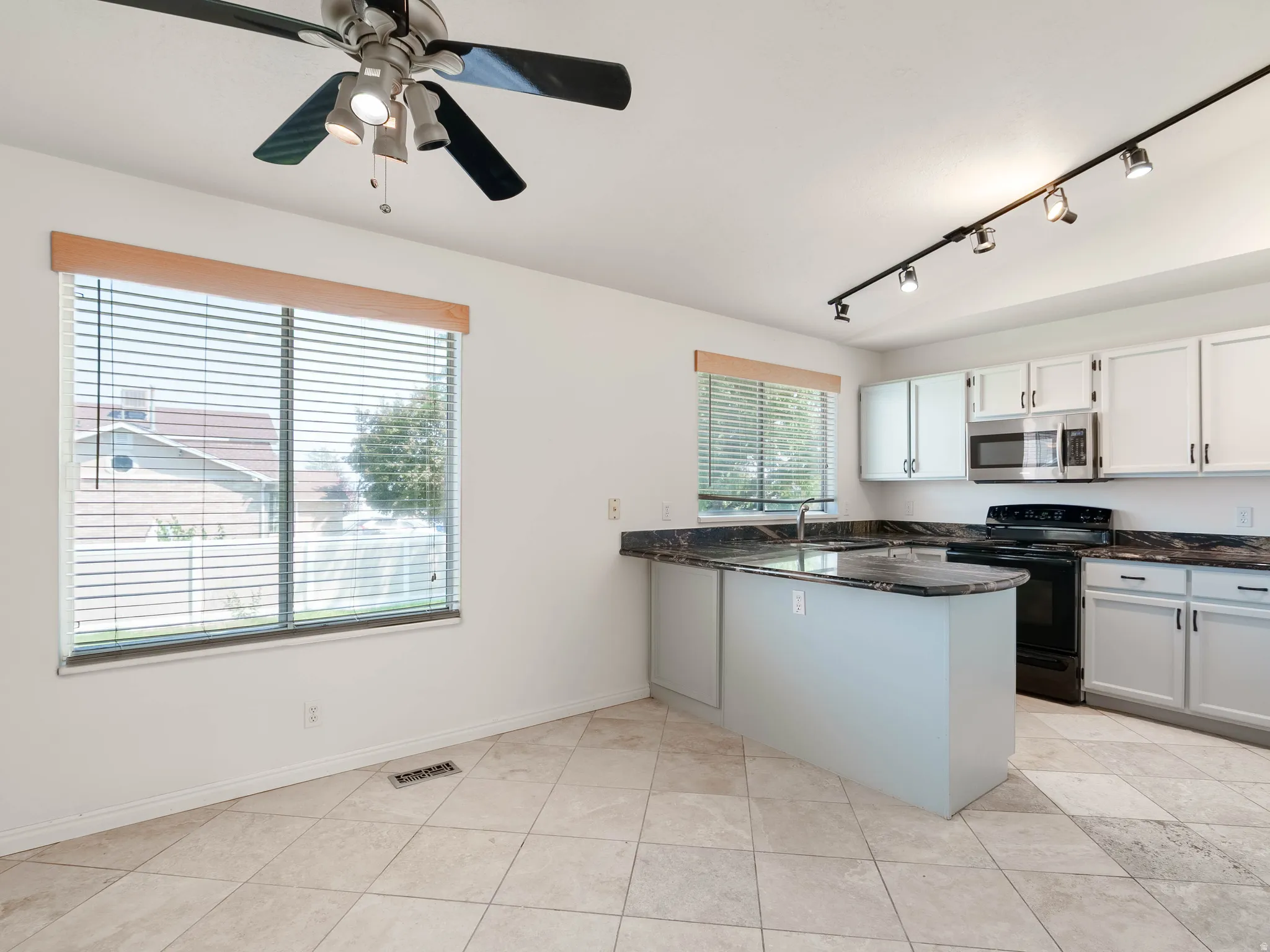 Kitchen featuring an island with a sink, white cabinetry, integrated stainless steel microwave, black electric range, and dark countertops