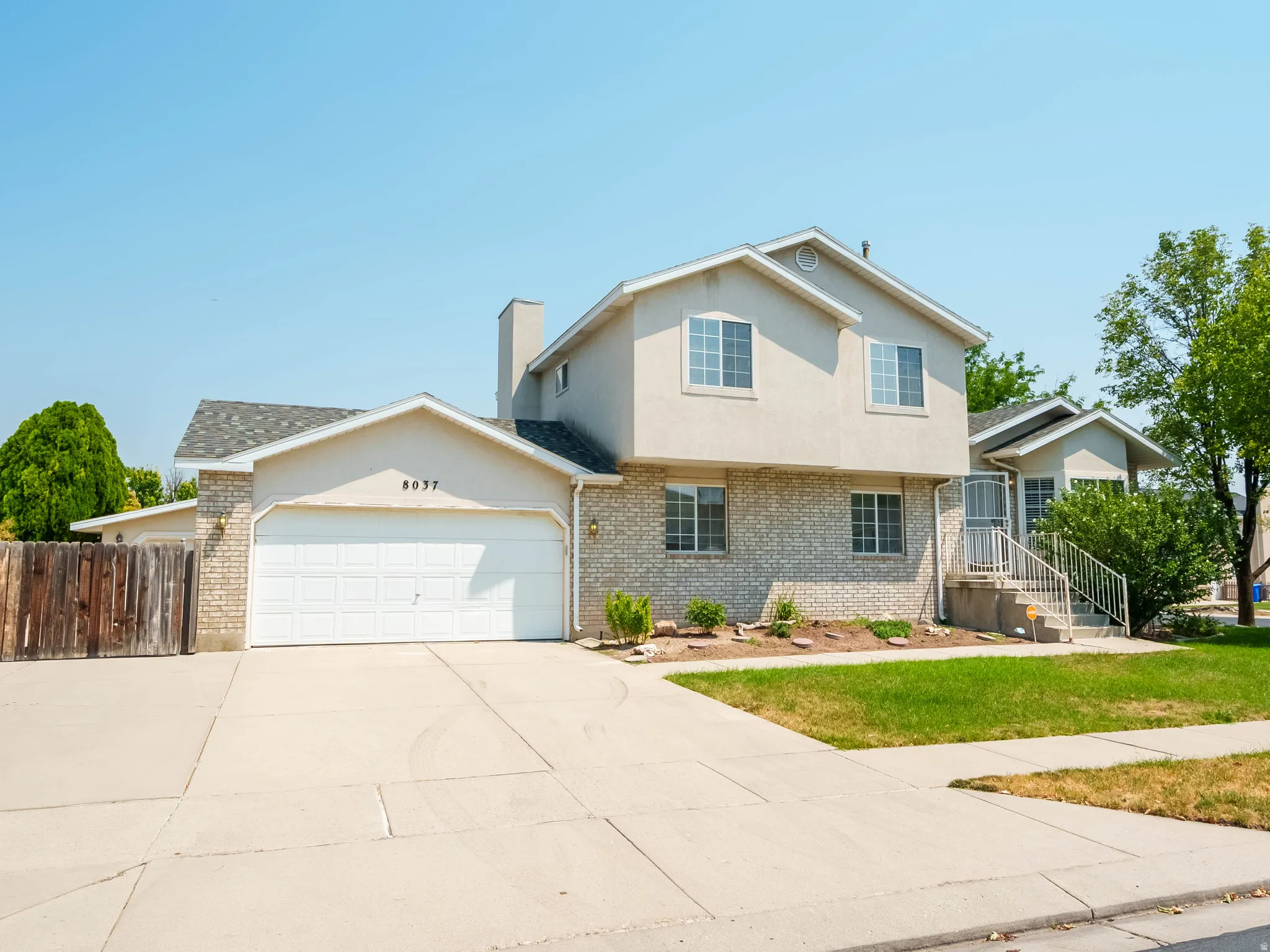 Two-story brick and stucco residence featuring a two-car attached garage with white overhead door, front-facing gable roofline with architectural detail, and a concrete driveway