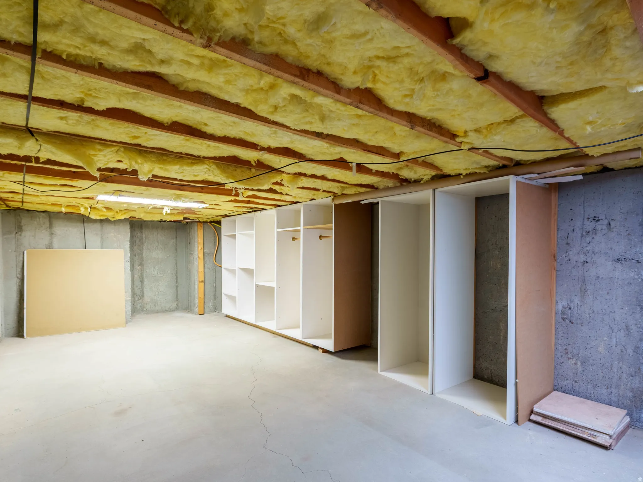 Basement storage area featuring built-in shelving units, concrete flooring, and exposed ceiling insulation