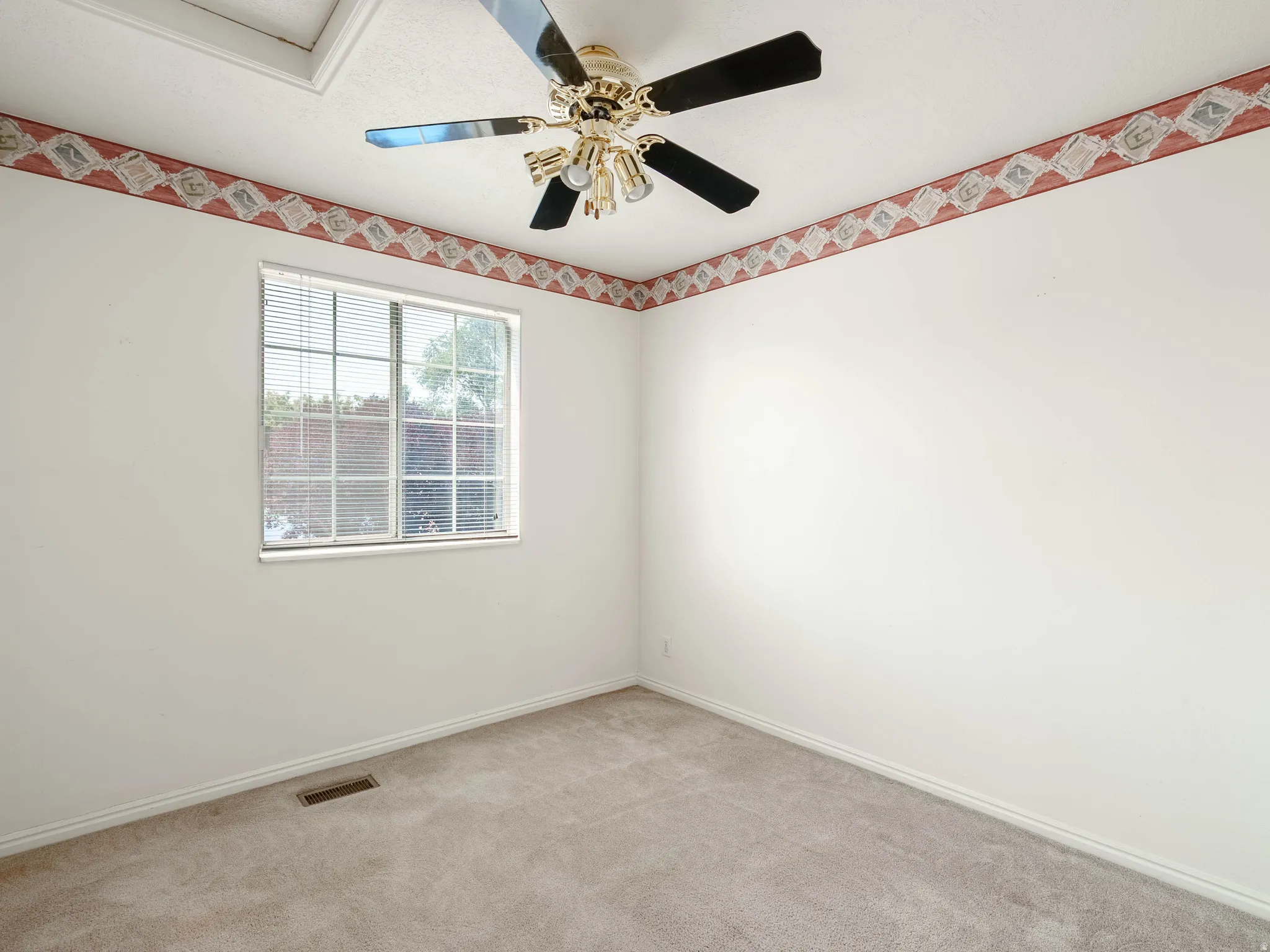 Carpeted room with a ceiling fan, a window with horizontal blinds, and a decorative border along the upper wall