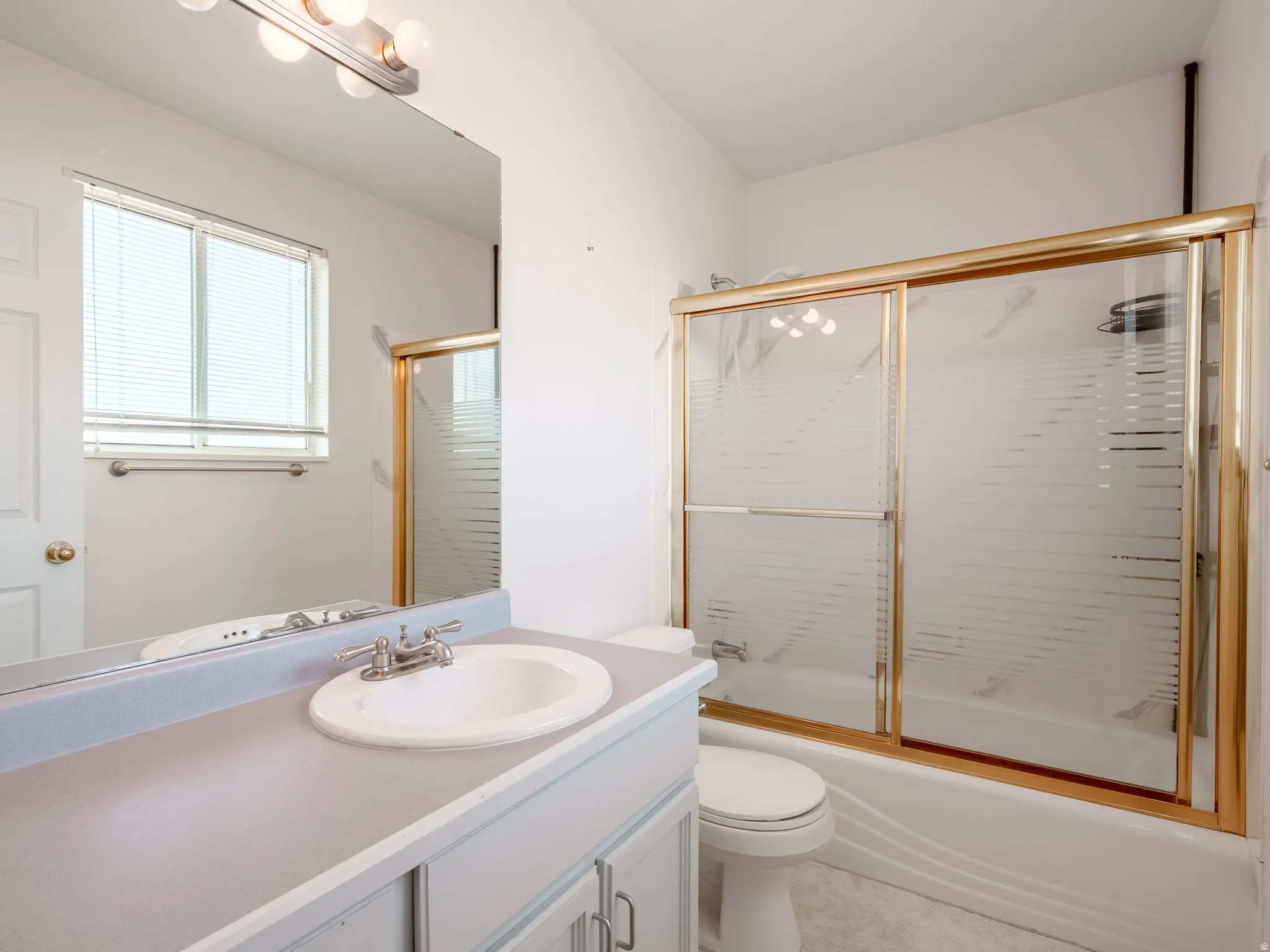 Integrated vanity with a single basin, gold-finish framed shower/tub combination, and built-in medicine cabinet