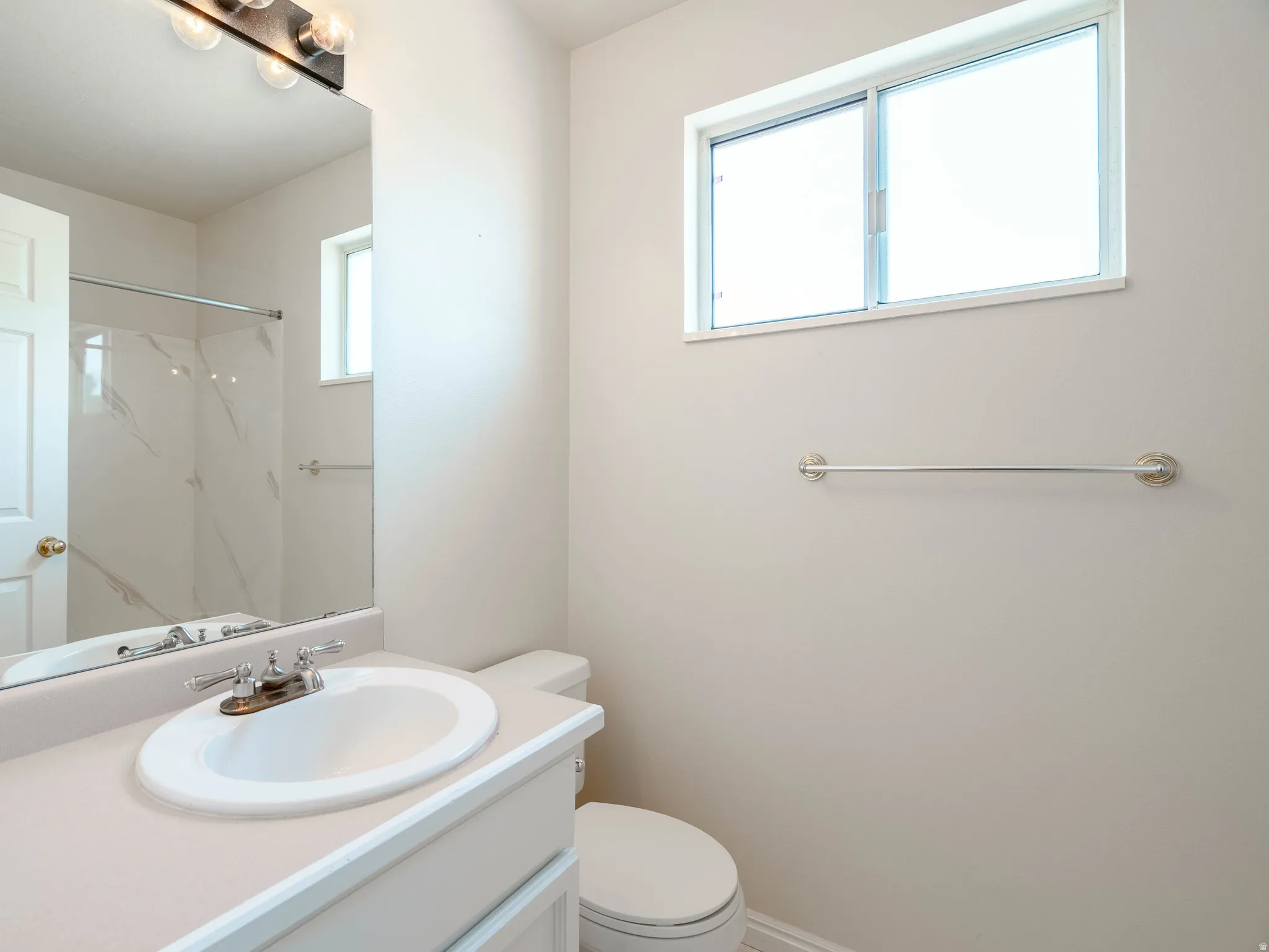 White vanity with an integrated sink, polished chrome faucet, built-in mirror, and overhead vanity lighting