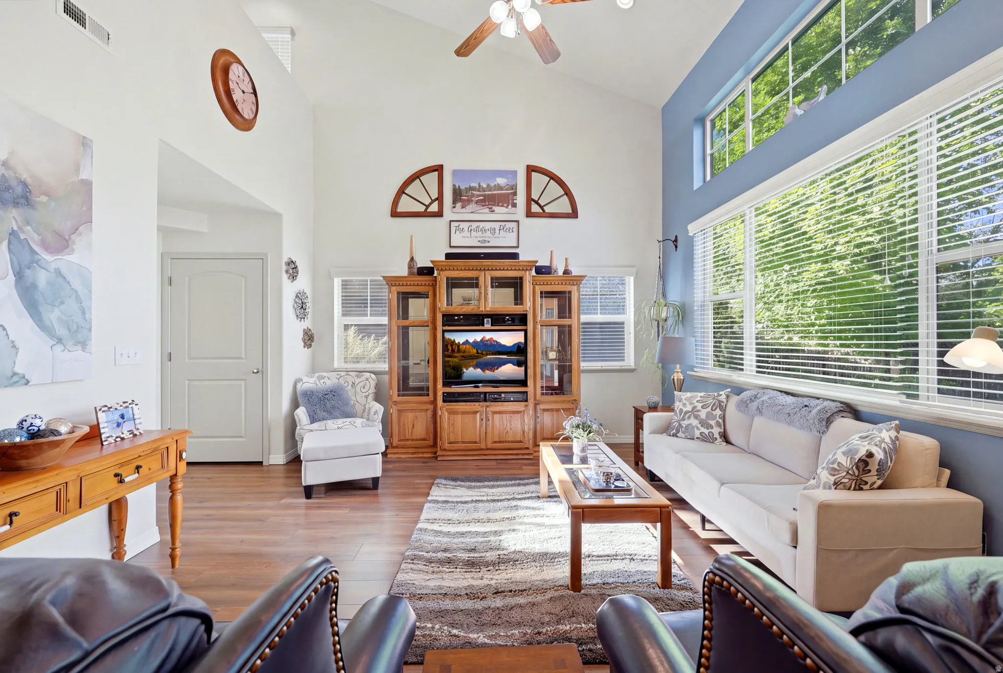 Vaulted ceilings with a ceiling fan, wood-finish flooring, built-in entertainment center, and expansive windows with upper transom windows