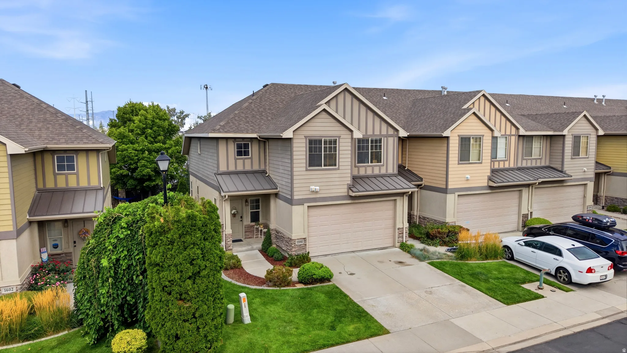 Multi-story townhome featuring a two-car garage, established landscaping, and a paved driveway
