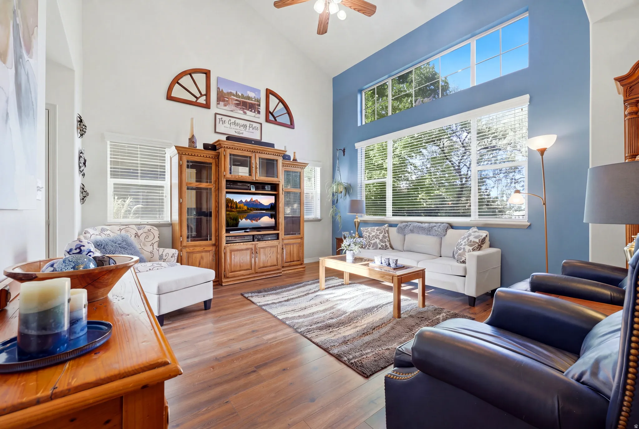 Vaulted ceiling with a ceiling fan, large picture windows, wood-finish flooring, and a built-in entertainment center