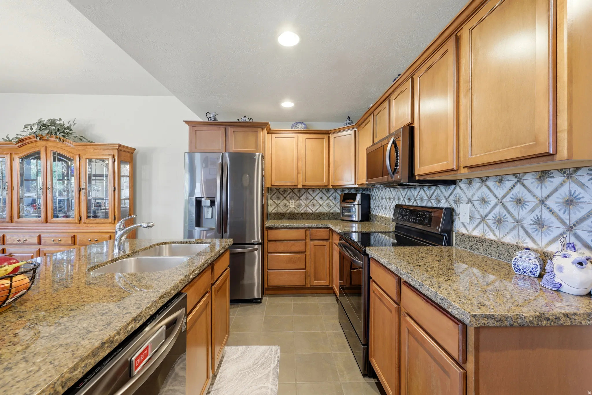 Kitchen featuring wood cabinetry, granite countertops, stainless steel refrigerator, stainless steel dishwasher, and patterned tile backsplash