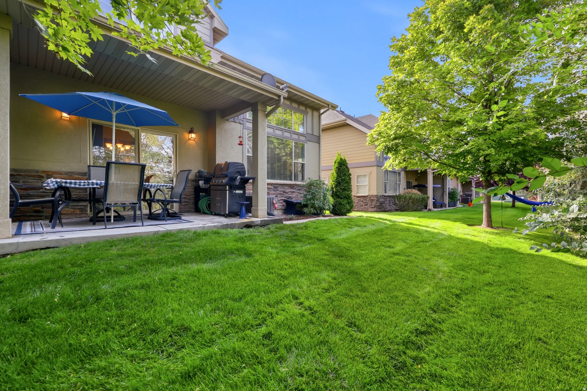 Covered patio with exterior wall sconces, stone veneer detailing, and a manicured lawn