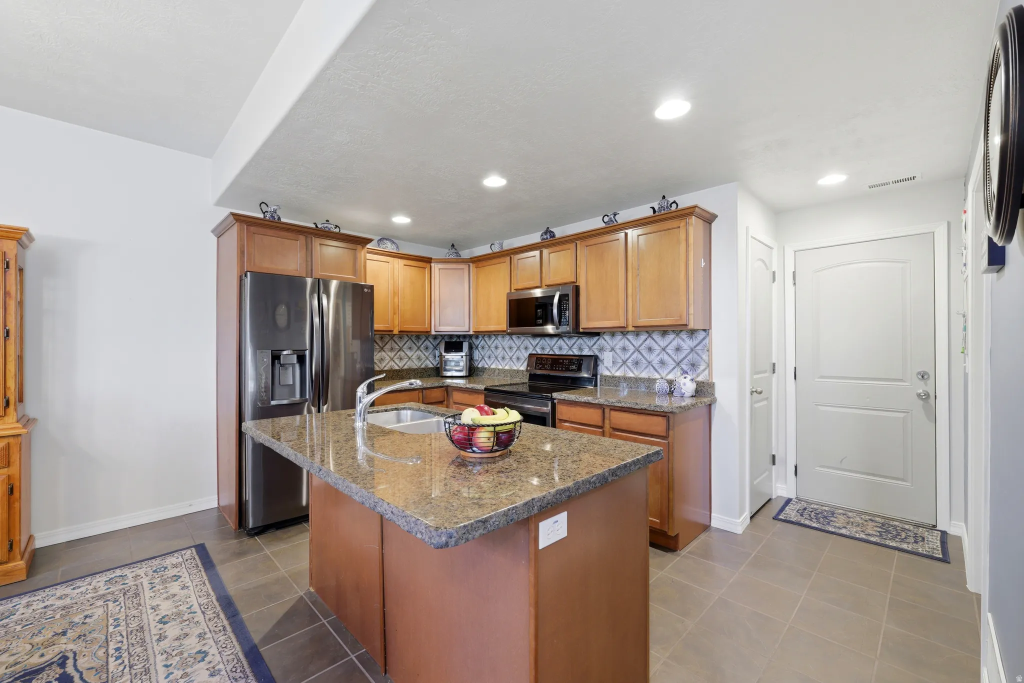 Kitchen featuring wood cabinetry, stainless steel appliances, a center island with a sink, and tile flooring