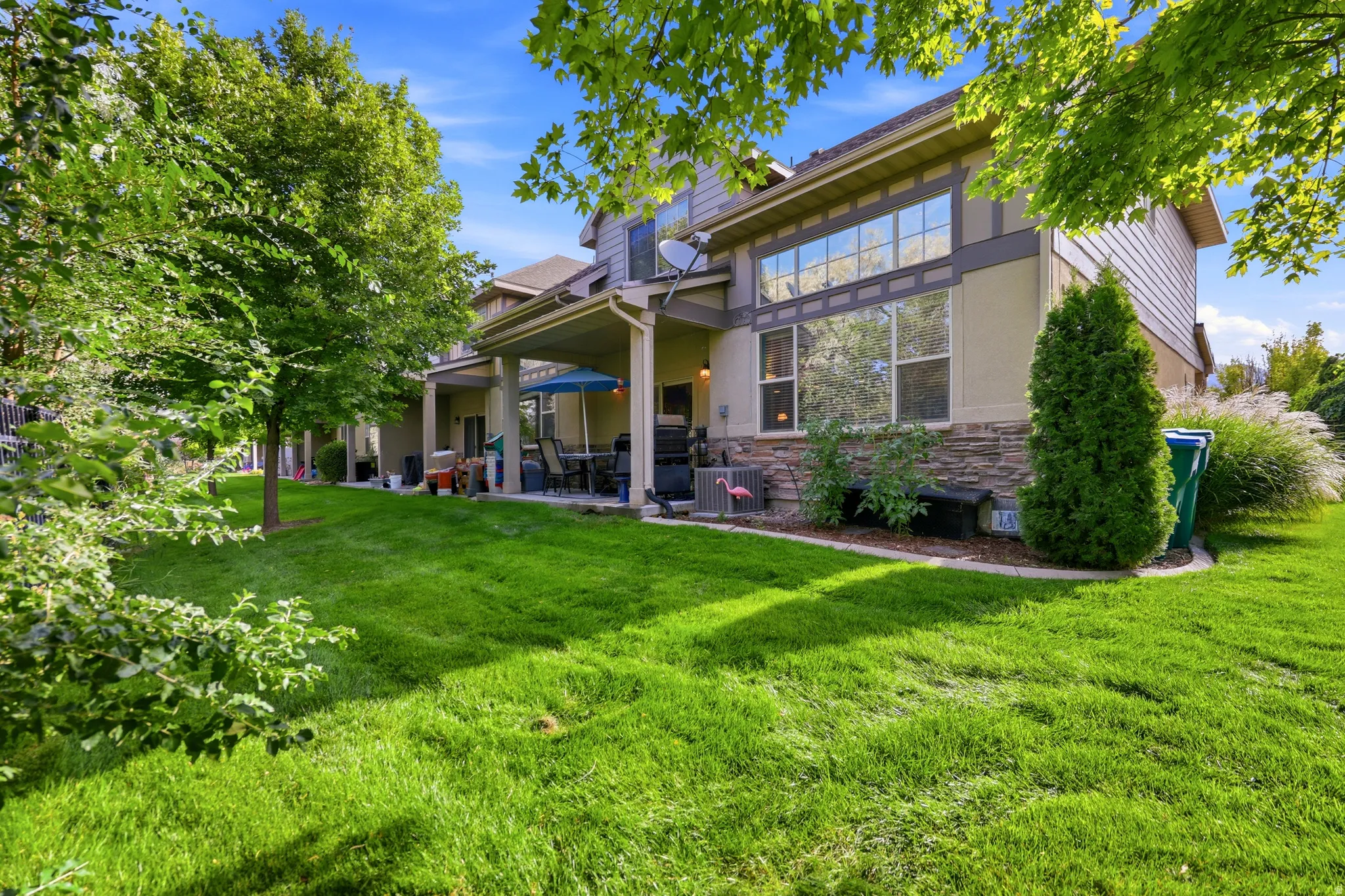 Expansive backyard featuring a manicured lawn, established shade trees, and a covered patio with direct access to the interior