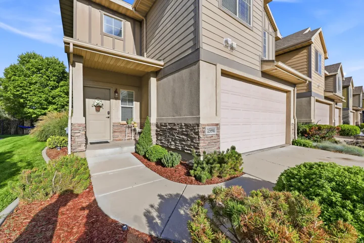 Exterior featuring siding and stone veneer, an attached garage, a covered entry, and a paved walkway