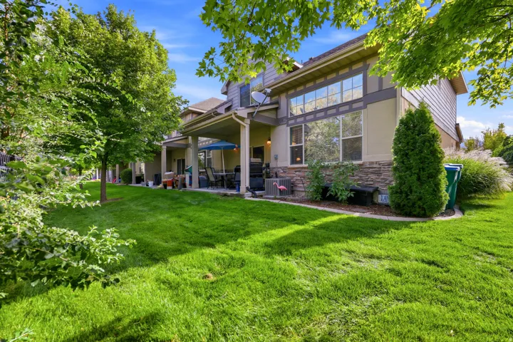 Expansive backyard featuring a manicured lawn, established shade trees, and a covered patio with direct access to the interior