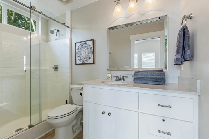 Spa-inspired ensuite bathroom featuring a frameless glass-enclosed shower with subway tile surround, white cabinetry with polished chrome hardware, a generous countertop with integrated sink, large illuminated mirror, and recessed and pendant lighting