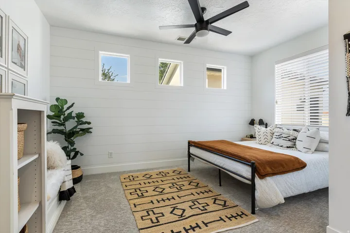 Bright bedroom featuring shiplap accent walls, large windows with plantation shutters, and ceiling fan