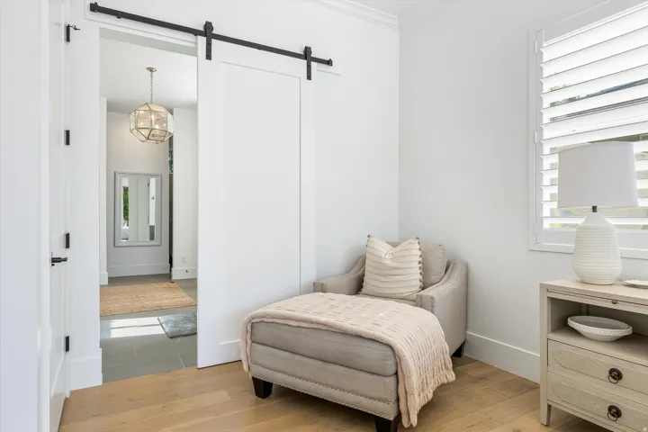 Bright bedroom showcasing hardwood flooring, barn-style sliding doors with black hardware, and a wooden nightstand with drawer storage