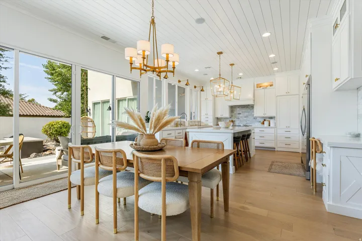 Bright open-concept kitchen and dining area featuring white cabinetry, stainless steel appliances, wood-finish flooring, and a large center island with seating