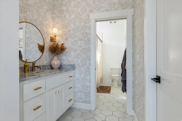 Elegant primary bathroom featuring a white shaker-style vanity with brass hardware, hexagonal tile flooring, and a decorative round mirror with brass frame