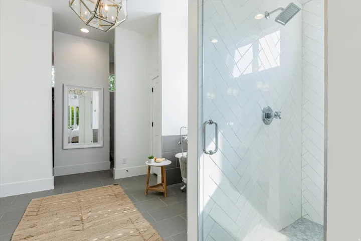 Primary bathroom featuring a frameless glass-enclosed shower with white subway tile surround, polished chrome fixtures, and rainfall showerhead