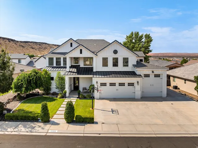 Modern farmhouse residence showcasing a clean white exterior with dark trim accents, dual garage doors, manicured front lawn with mature landscaping, circular driveway with stamped concrete finish, and gabled roofline with architectural detailing set agai
