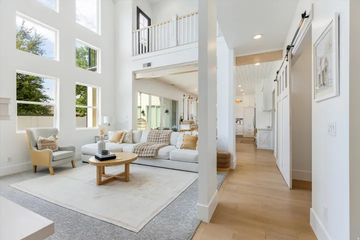 Soaring two-story foyer with abundant natural light from multi-pane windows, hardwood flooring, and an open-concept layout anchored by a wood-frame coffee table base