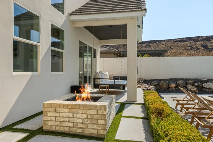 Modern outdoor entertaining space featuring a custom brick fire pit with clean lines, manicured lawn with linear hedging, stamped concrete hardscaping, and direct access to the residence through a covered pavilion with clerestory windows