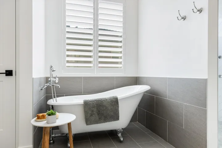 Spa-inspired bathroom featuring a freestanding soaking tub with chrome claw feet, polished chrome deck-mounted faucet with handheld showerhead, and horizontal stacked tile wainscoting in charcoal gray