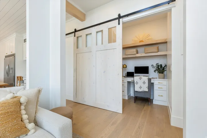 Bright home office alcove featuring built-in white cabinetry with drawer storage, wood-finish flooring, and barn-style sliding doors