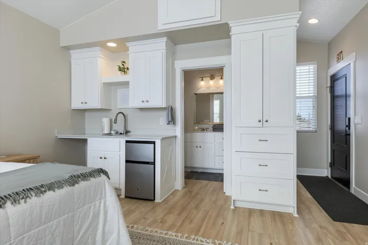 Primary bedroom suite featuring custom white cabinetry with ample storage, wood-finish flooring throughout, stainless steel appliances, and an ensuite bathroom with recessed lighting and dual vanity