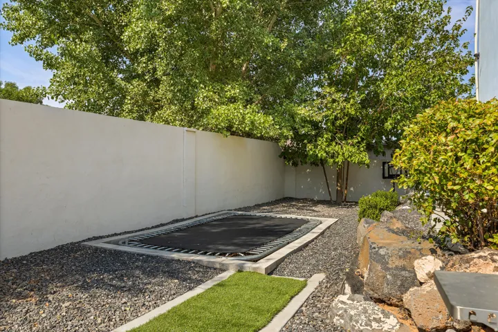 Enclosed outdoor space featuring a built-in ground-level trampoline, gravel landscaping, and mature trees