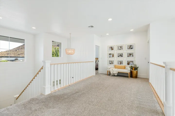 Spacious loft-style landing featuring gleaming wood-finish railings, recessed lighting, and neutral carpet flooring