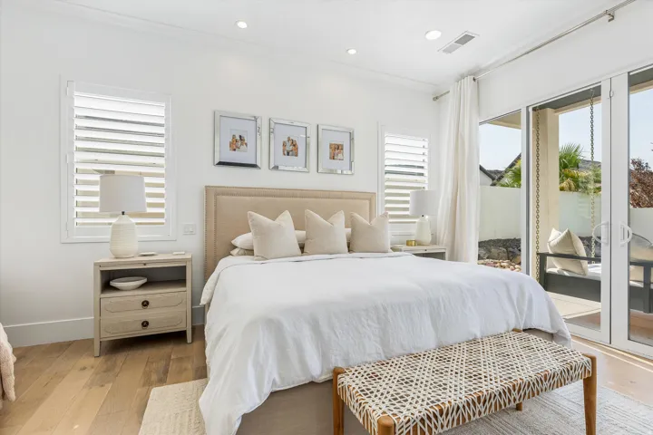 Bright primary bedroom showcasing a wood-finish upholstered headboard, white bedding, and natural light from dual glass sliding doors opening to a private balcony
