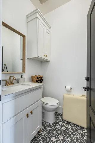 Elegant powder room featuring crisp white cabinetry with brass hardware, a streamlined vanity with integrated sink and quartz countertop, polished chrome faucet, and a geometric patterned tile floor in black and white